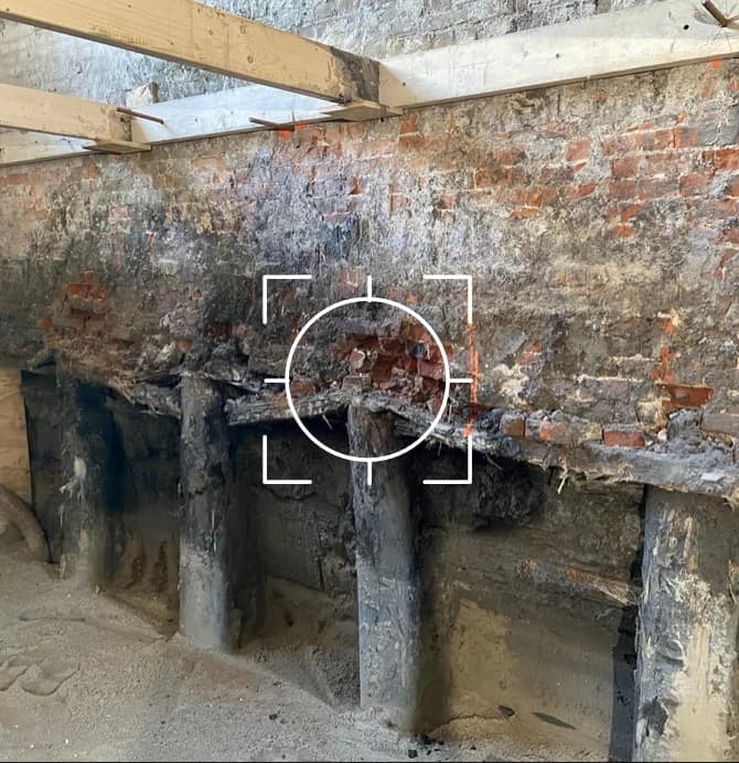 Aangetaste houten paalfundering onder een gemetselde muur